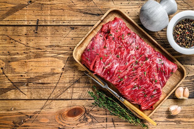 Raw beef round cut meat on a wooden tray with herbs. wooden background. Top view. Copy space.