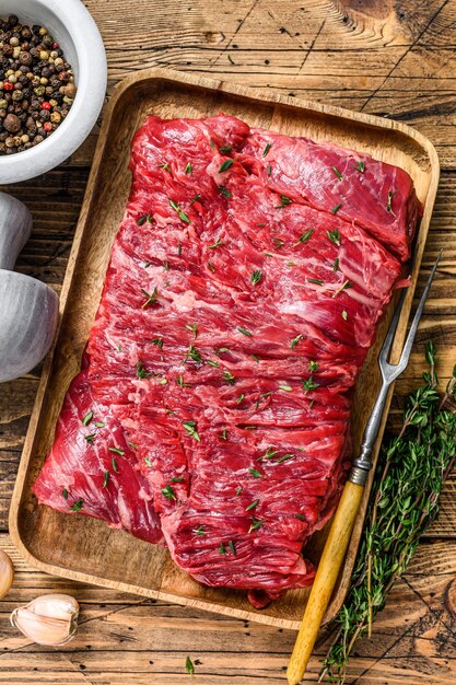 Raw beef round cut meat on a wooden tray with herbs