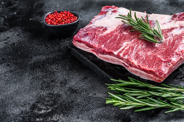 Raw beef short ribs kalbi on marble board. Black background. Top view. Copy space.