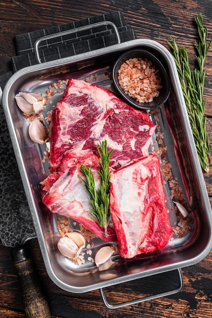 Raw beef Short Ribs in steel tray with rosemary. Wooden background. Top view.