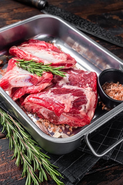 Raw beef short ribs in steel tray with rosemary wooden\
background top view