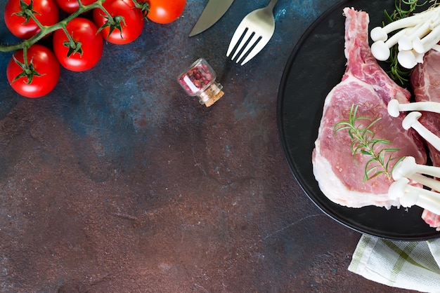 Photo raw beef steak on the bone with fresh vegetables in a grill pan on a concrete surface