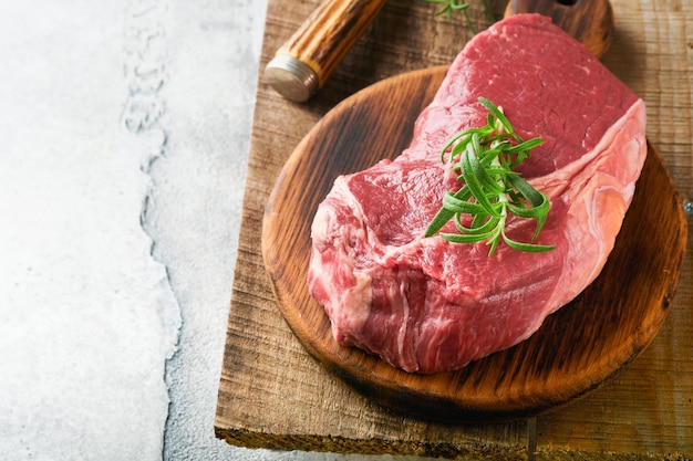 Raw beef steak Fresh beef rib eye steak with fork rosemary salt and pepper on piece of parchment paper on old wooden background Top view Mockup for design idea