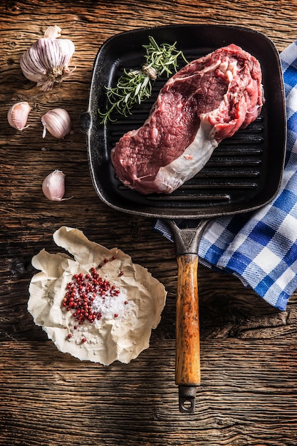 Bistecca di manzo cruda in padella con sale pepe aglio ed erbe sul tavolo di legno.