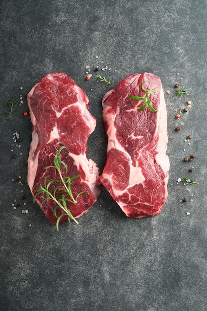 Raw beef steak Marbled raw fresh Ribeye steak with rosemary salt and pepper on cutting board on dark concrete background Raw beef steak and spices for cooking