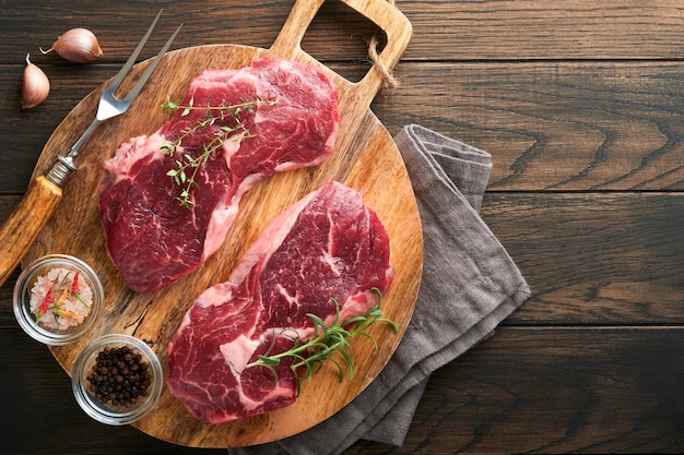 Raw beef steak Marbled raw fresh Ribeye steak with rosemary salt and pepper on cutting board on dark concrete background Raw beef steak and spices for cooking