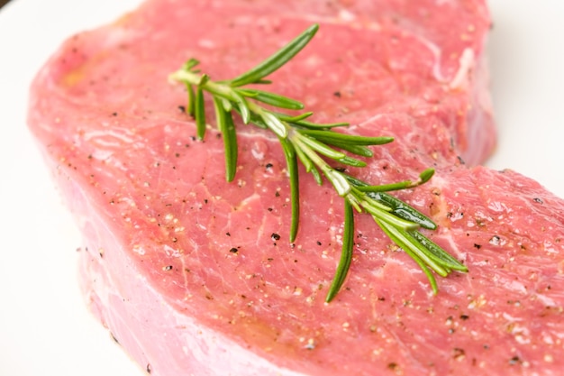 Raw beef steak meat with branch of rosemary and species isolated on a white background.