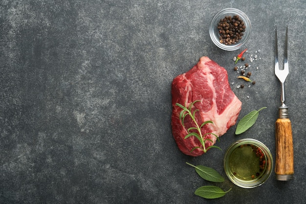 Raw beef steak raw fresh chuck roll steak with rosemary salt\
and pepper on cutting board on dark concrete background raw beef\
steak and spices for cooking