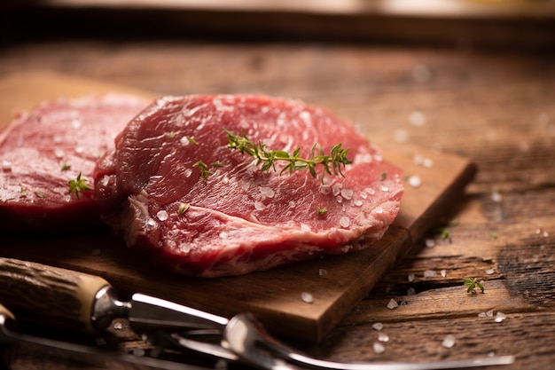 Raw beef steak and spices on wooden cutting board close up