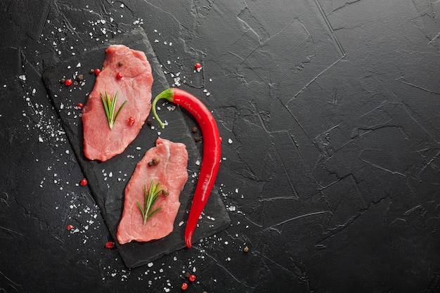 Raw beef steak with rosemary and peppers on dark stone