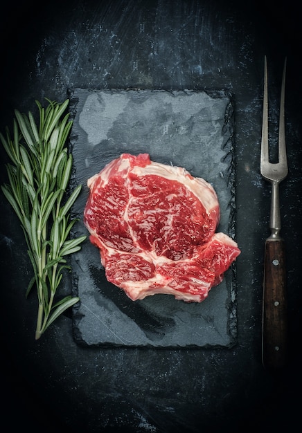 Raw beef steak with rosemary on stone plate.