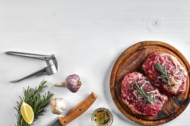 Photo raw beef steak with spices and ingredients for cooking on wooden cutting board and white background