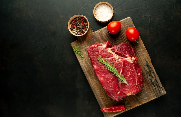 raw beef steak with spices and rosemary on a stone background with copy space for your text