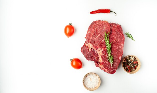 raw beef steak with spices and rosemary on a white plate