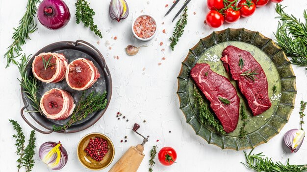 Raw beef steaks on over metal tray with spices light background. top view.