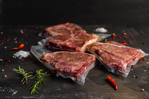 Raw beef steaks in plastic bags with rosemary and spices on a black background.
