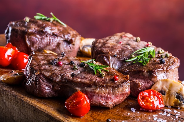 Raw beef steaks on wooden board with spices and herbs.