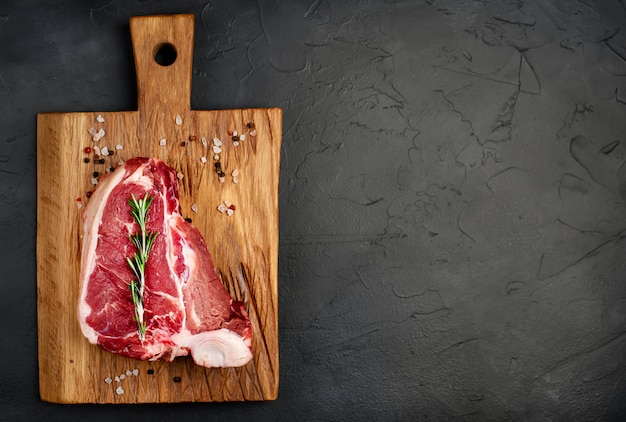 Raw beef t-bone steak on a cutting board with spices on the background  stone. with copy space for your text.