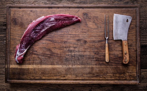 Raw beef tenderloin steak on a cutting board with rosemary pepper salt in other positions