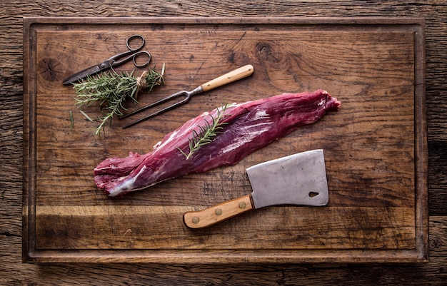 Raw beef tenderloin steak on a cutting board with rosemary pepper salt in other positions