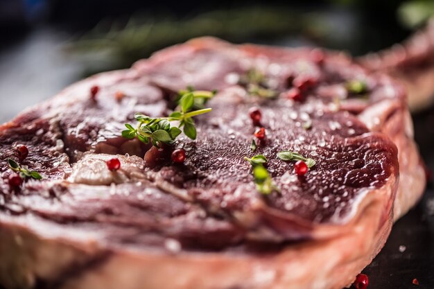 Raw beef tomahawk steak with salt pepper and rosemary on slate plate.