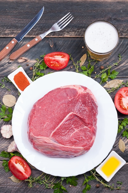 Raw beef with herbs, spices, vegetables and beer in a glass on a wooden background