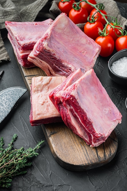 Raw Black Angus Marbled Beef Ribs set, met ingrediënten, op zwarte stenen achtergrond