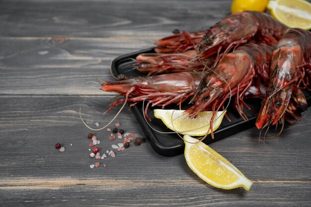 Raw black tiger shrimps on black plate and wood table decorated with lemon slices