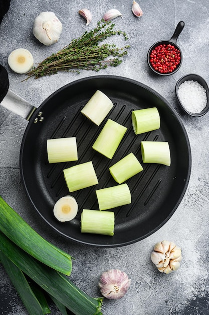 Raw braised leeks on grill pan uncooked with herbs ingredients\
on textured grey background top view