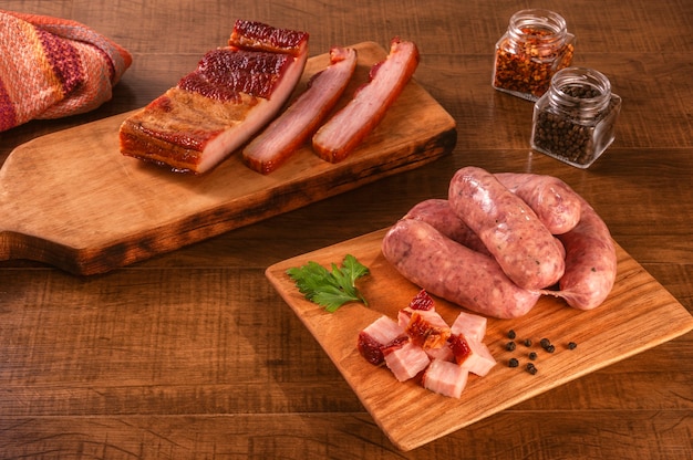 Raw brazilian bacon sausages on the wooden board with fresh cubes of bacon and spices