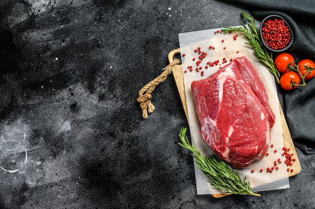 Il manzo di petto crudo ha tagliato su un tagliere di legno sul manzo di angus nero sulla tavola nera