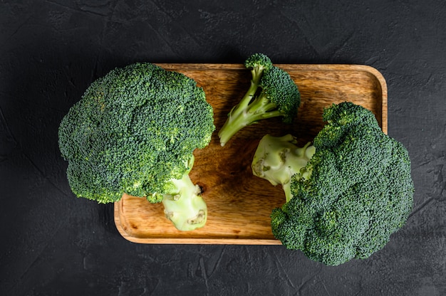 Raw broccoli in a wooden bowl. Black background. Top view