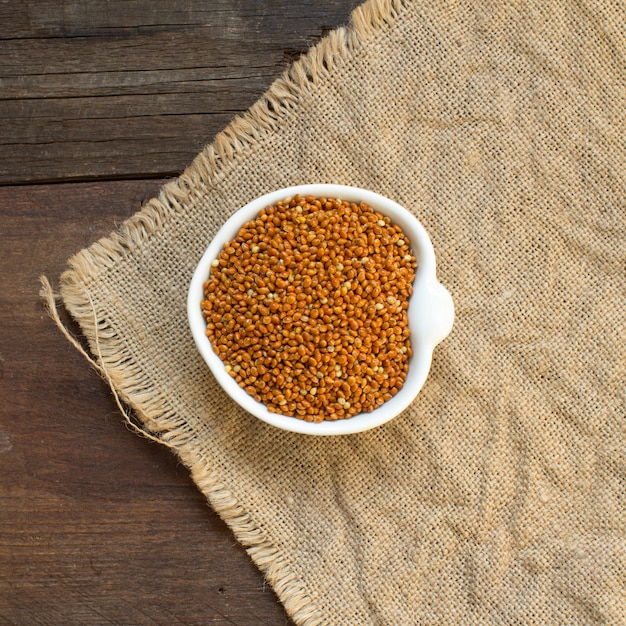 Raw brown millet in a bowl on burlap and wood, top view
