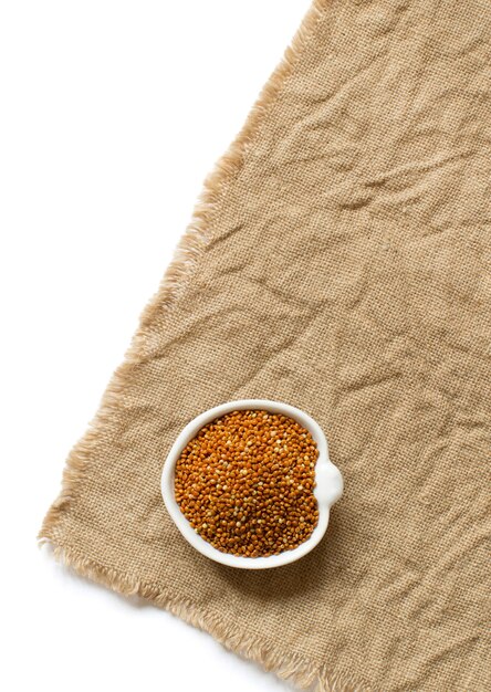 Raw brown millet in a bowl on burlap and wood