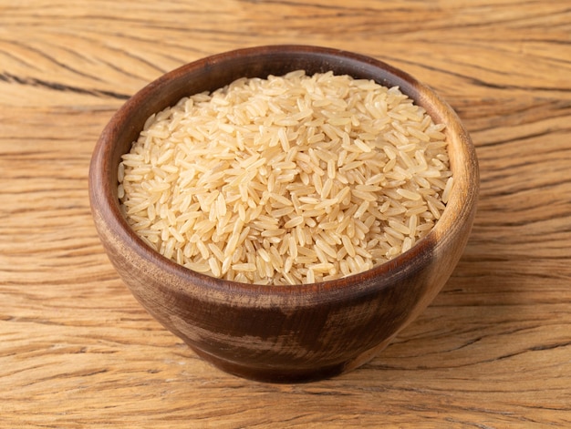 Сырой коричневый цельный рис в миске над деревянным столом.