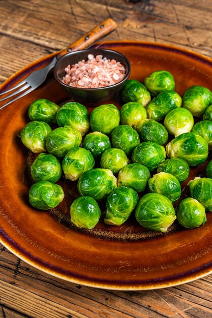 Raw brussels green sprouts cabbage in a rustic plate with salt. wooden background. top view