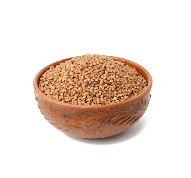 Raw buckwheat grains in brown ceramic plate, cereals isolated