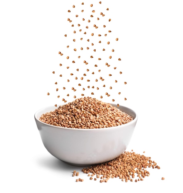 Raw buckwheat grains falling in bowl on white background