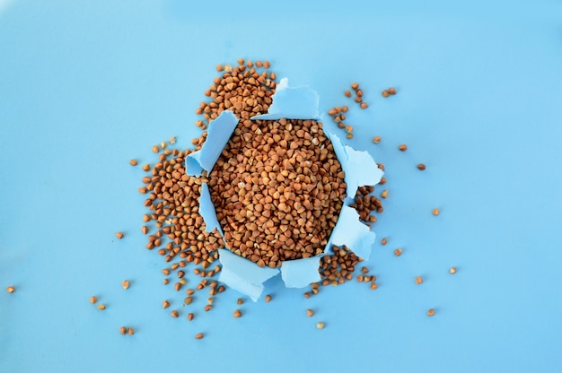 Raw buckwheat peeking out of a paper hole on blue