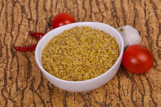 Raw bulgur in the bowl with tomatoes and garlic