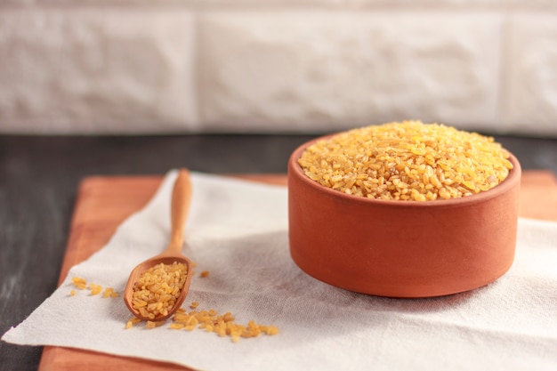 Raw bulgur in a clay bowl on a wooden board