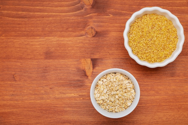 Raw bulgur, oak flakes in white bowls.