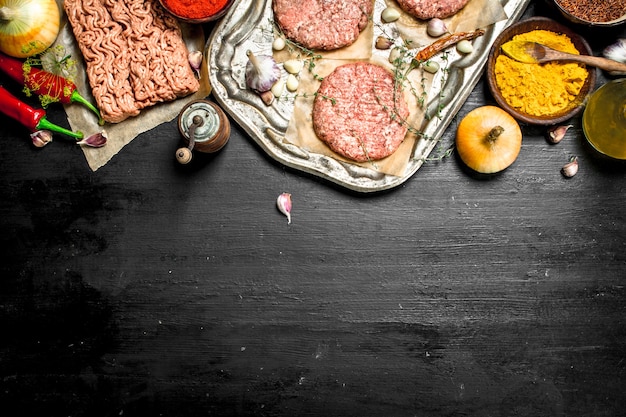 Hamburger crudo con aglio e spezie su un vassoio in acciaio.