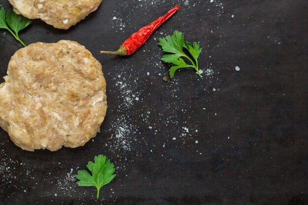 Hamburger crudi - cotolette di carne di pollo con prezzemolo e peperoncino su sfondo nero, vista dall'alto