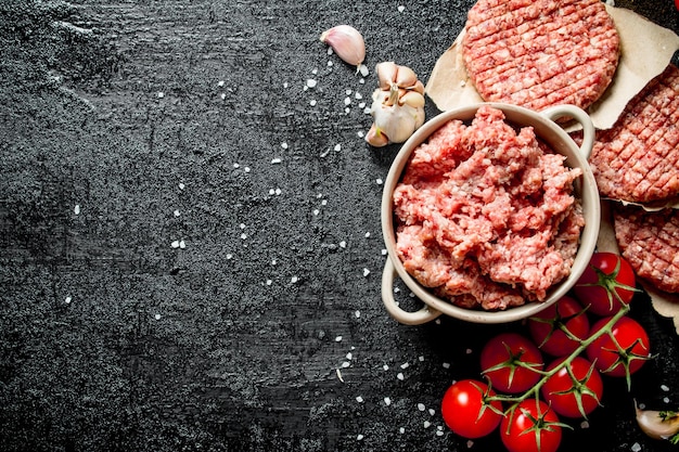 Raw burgers and ground beef with cherry tomatoes and garlic