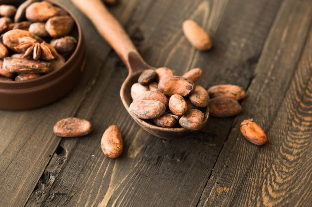 Raw cacao beans in burlap bag and bowl with cacao powder on a wooden table