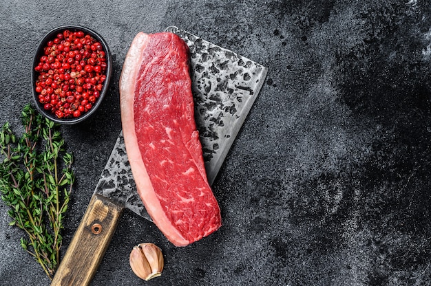 Raw cap rump beef meat steak on a butcher cleaver on wooden table. Top view.