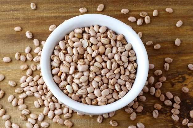 Raw carioca beans in bowl over rustic wooden table Product name in Brazilian Portuguese Top view