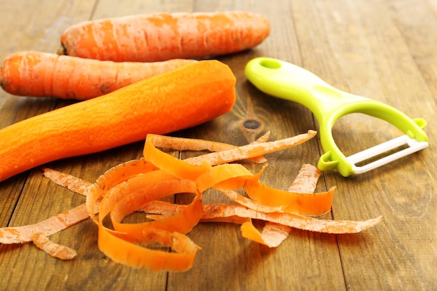 Raw carrots and peeler on wooden table