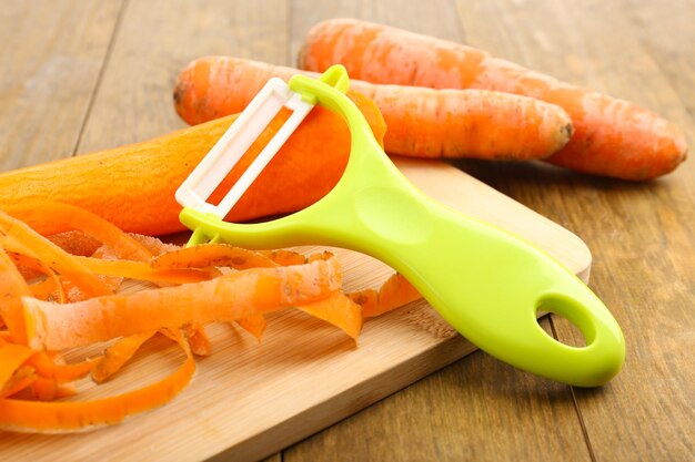 Raw carrots and peeler on wooden table